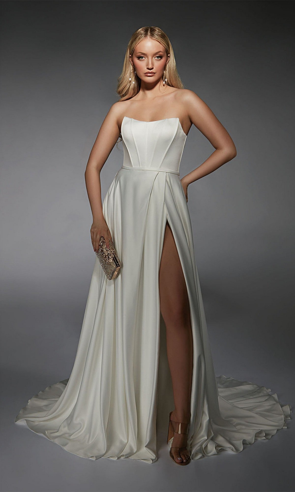 A woman elegantly poses against a plain gray backdrop, wearing the Alyce 7111 long white dress with a strapless satin bodice and an a-line skirt, and holding a clutch.